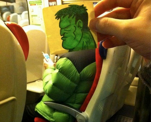 A person on a train with a drawing of the Hulks face held in front of their face