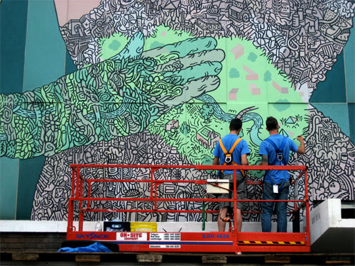 Two men in forklift painting mural.